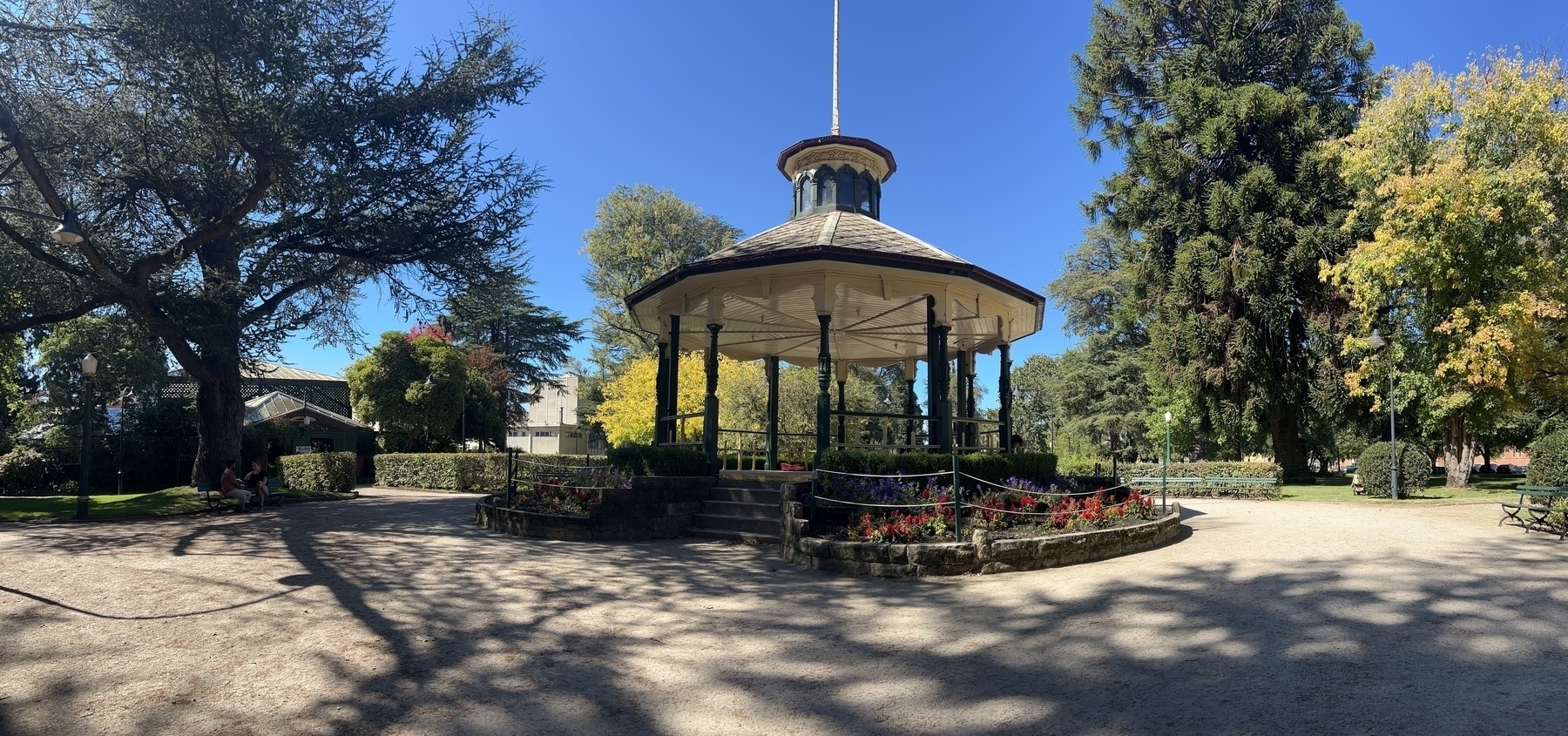 A panoramic photo of a park with trees and deep blue skies. I rotunda is in the foreground. 
