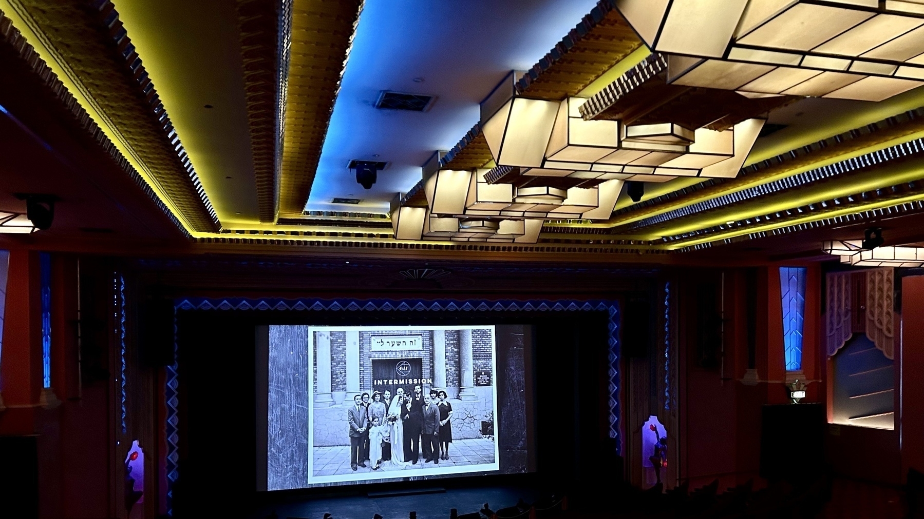 A large, old cinema. On the screen is a greyscale photo of a family and the word Intermission. It’s from the intermission in The Brutalist (2024). 