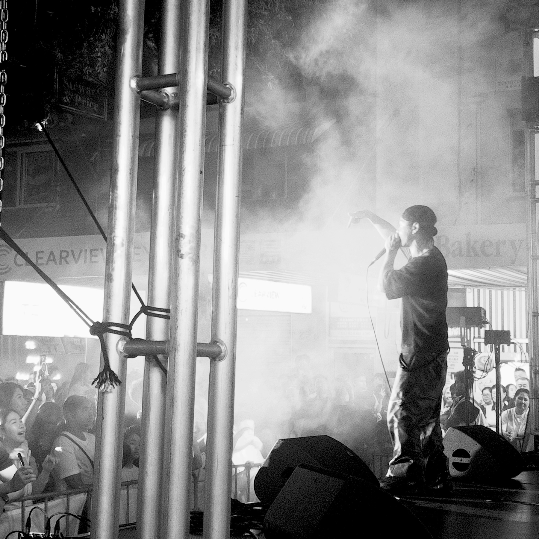 A performer on stage sings into a microphone amid hazy lighting and a cheering crowd.