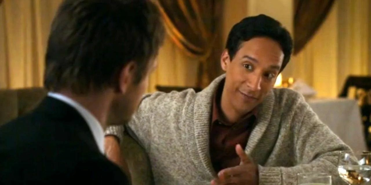 Two people are sitting at a table, engaged in conversation, with one gesturing expressively while wearing a cozy sweater.Two men sit across from each other at a small restaurant table in warm, low lighting. The man on the left is seen in soft focus from behind, wearing a dark suit, while the man on the right, in a light grey cardigan, leans forward with an attentive, slightly amused expression. A glass of white wine and simple table setting sit between them, with heavy curtains and golden tones in the background creating an intimate, composed atmosphere. This image is from the Community episode “My Dinner with Abed,” which deliberately mirrors the style and structure of the film My Dinner with Andre - focusing on extended, introspective conversation over dinner, with visual emphasis on subtle facial expressions, body language, and the rhythm of dialogue rather than action.